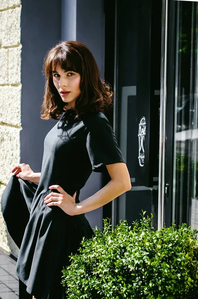 Karanlık bir şık elbiseli güzel kadın butikler yakınındaki cadde boyunca elini kolunu sallaya dönüyor. Bir moda kız portresi