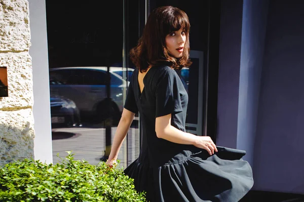 Karanlık bir şık elbiseli güzel kadın butikler yakınındaki cadde boyunca elini kolunu sallaya dönüyor. Bir moda kız portresi