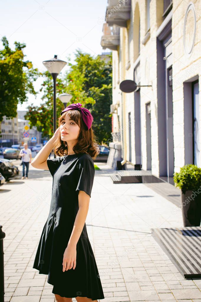 Beautiful woman in a dark stylish dress strolls along the street, near boutiques. Portrait of a fashionable girl