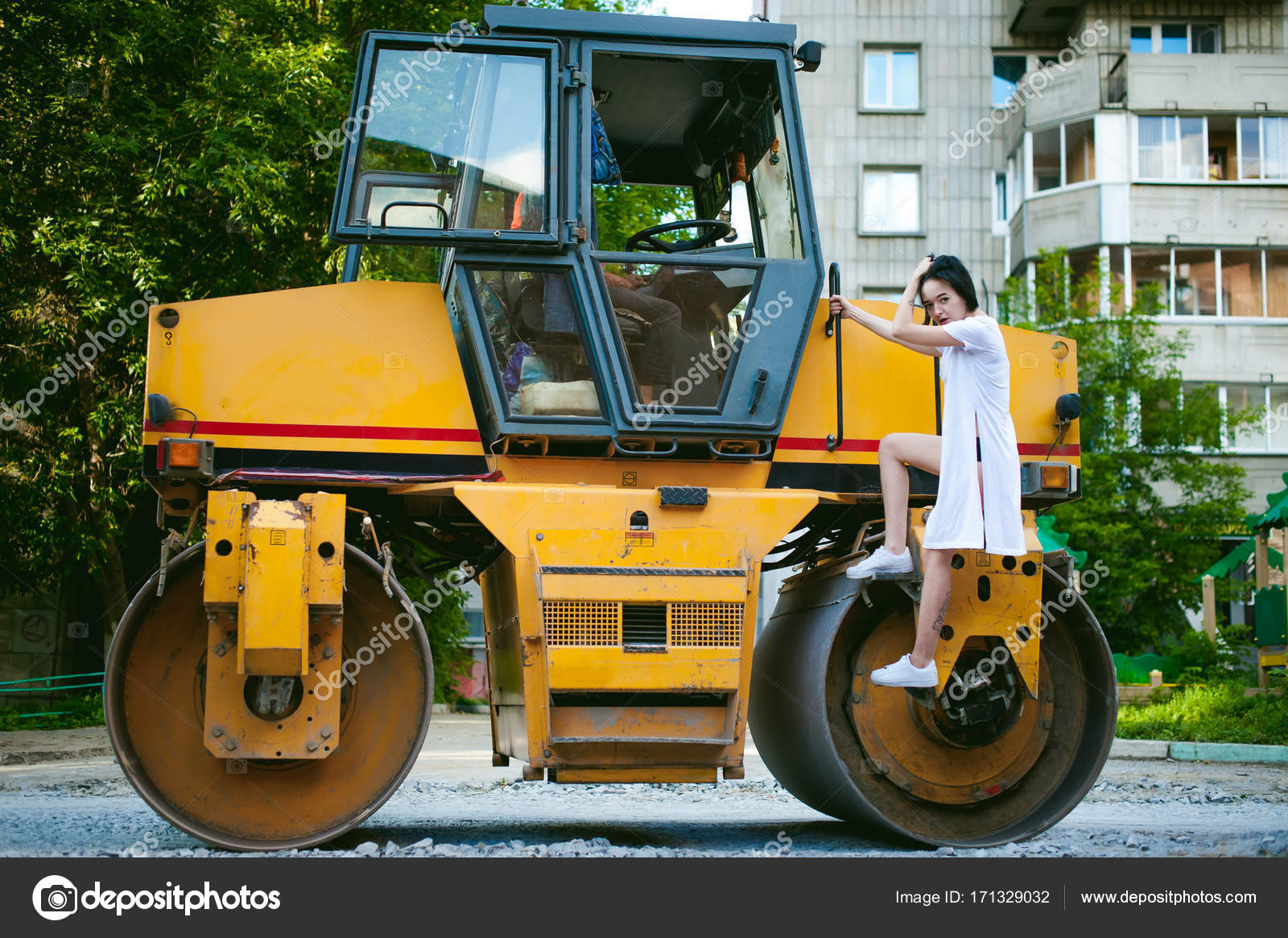 Young Woman With Bare Feet Dressed In White Sneakers And A Long Jersey Against A Backdrop Of Urban Landscapes And Road Machinery Asphalt Paver Young Woman With Bare Feet Dressed In White Sneakers And A Long Jersey Against A Backdrop Of Urban Landscapes And Road Machinery Asphalt Paver