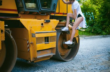 çıplak ayak beyaz spor ayakkabı, yol makine, asfalt finişer ve kentsel manzara fonunda uzun bir forma giymiş olan kadın. Sokak moda.