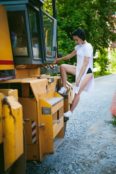 흰색 운동 화와 도시 경관과로 기계, 아스팔트 포장 재료의 배경 긴 셔츠를 입은 맨발으로 젊은 여자. 스트리트 패션. — 스톡 사진