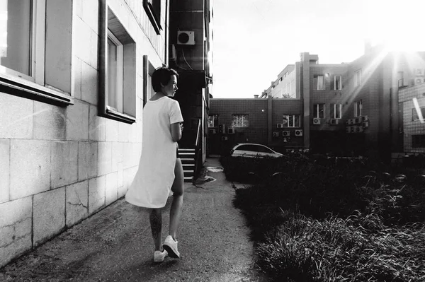 年轻女子裸腿穿着白色运动鞋和长 t恤, 在城市的背景下 — 图库照片
