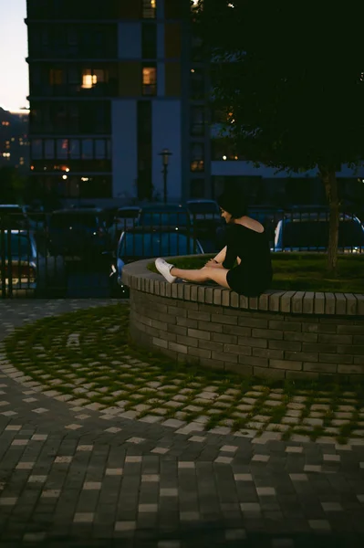 Jonge vrouw met mooie voeten gekleed in witte sneakers en zwarte jurk, tegen een achtergrond van stedelijke landschappen — Stockfoto