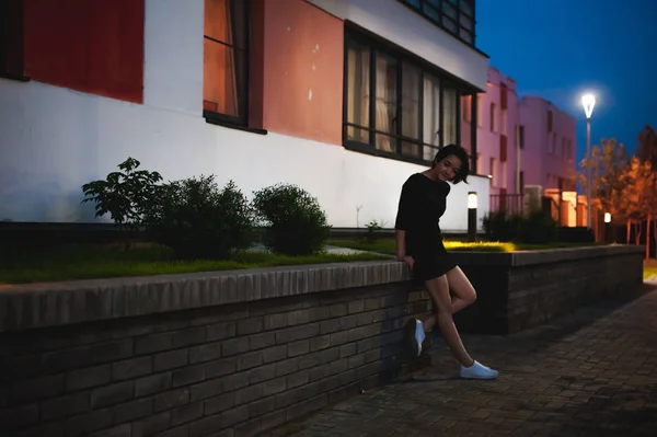 Jovem com belos pés vestidos de tênis branco e vestido preto, contra um pano de fundo de paisagens urbanas — Fotografia de Stock