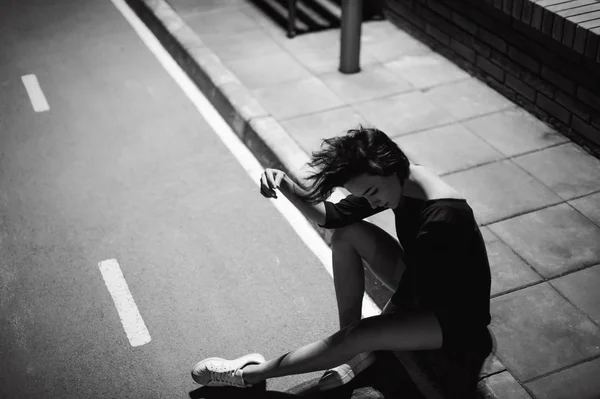 Young woman with beautiful feet dressed in white sneakers and black dress, against a backdrop of urban landscapes — Stock Photo, Image