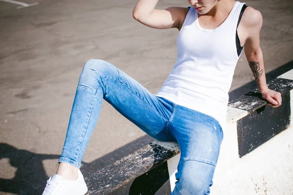 Mujer joven vestida con zapatillas blancas, una camiseta y vaqueros azules, contra el telón de fondo de paisajes urbanos. Moda callejera — Foto de Stock