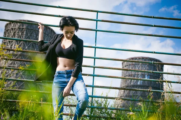 Mujer joven vestida con zapatillas blancas, top negro y jeans azules, sobre un fondo de paisajes urbanos. Moda callejera — Foto de Stock