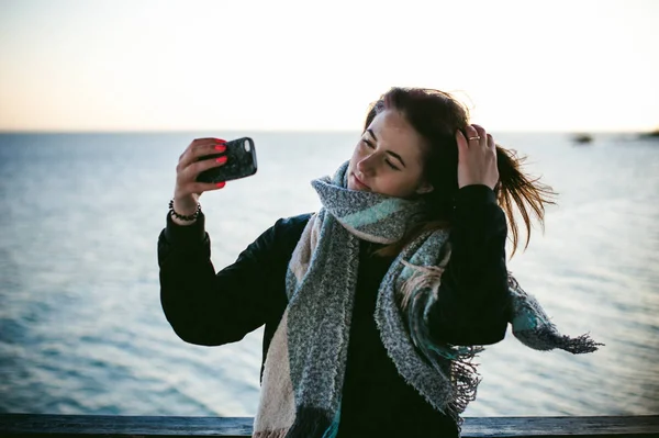 ビーチでのスカーフに包まれた寒い日に女性が携帯電話で写真を取る — ストック写真