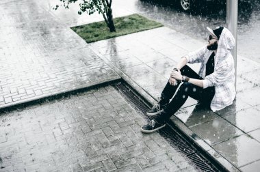 mahallede bir kap ve serbestçe şehirde yürüyüş güneş gözlüğü ile hafif kareli ceket içinde sakallı genç adam yağmur yere oturur