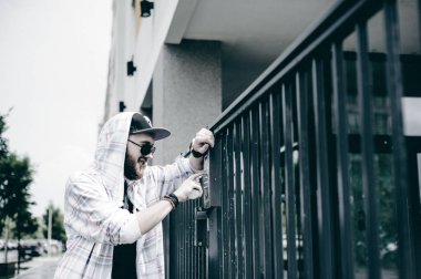 interkom aramak için çift sayı tuş takımındaki hood bir şapka ve güneş gözlüğü ile hafif kareli ceket içinde sakallı genç adam alır