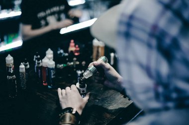 mahallede bir kap ile hafif kareli ceket içinde sakallı genç adam vape çubuğunda elektronik sigara içiyor