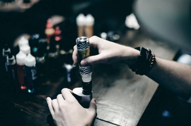 mahallede bir kap ile hafif kareli ceket içinde sakallı genç adam vape çubuğunda elektronik sigara içiyor