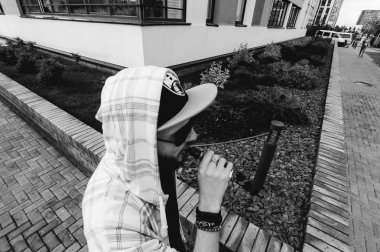 Kapüşonlu, kapüşonlu ve güneş gözlüklü sakallı genç adam şehirde serbestçe dolaşıyor ve bir e-sigara içiyor.