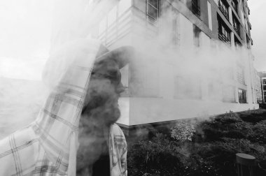 Kapüşonlu, kapüşonlu ve güneş gözlüklü sakallı genç adam şehirde serbestçe dolaşıyor ve bir e-sigara içiyor.