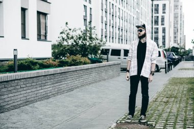 Kapüşonlu, kapüşonlu ve güneş gözlüklü sakallı genç adam şehirde serbestçe dolaşıyor ve bir e-sigara içiyor.