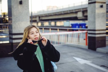 genç kadın bir kürk ceket, bir kazak ve kulaklı, moda güneş gözlüğü bir sırt çantası ile şehir etrafında elini kolunu sallaya dönüyor. Sokak moda