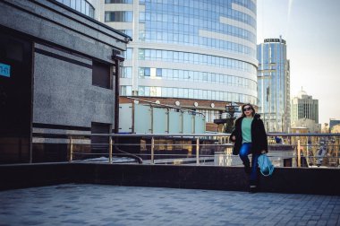 genç kadın bir kürk ceket, bir kazak ve kulaklı, moda güneş gözlüğü bir sırt çantası ile şehir etrafında elini kolunu sallaya dönüyor. Sokak moda