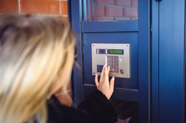 Genç sarışın kadın kürk ceket, doorphone panel kodu çeviren, evin içine girebilmen için parmaklarını ile düğmeleri presler