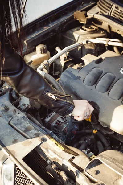 brunette woman in black fashionable leather clothes on style, auto lady. looks under the hood of the car on the engine, the problem needs repair