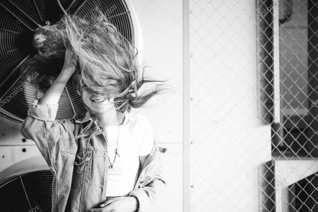 street portrait of a young attractive emotional girl with curly hair dressed in a trendy denim suit on the style. against the background of air conditioner ventilator systems. the wind in her hair