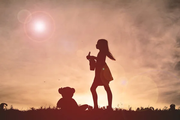 Silhouette fille jouer musical avec ours en peluche au coucher du soleil — Photo