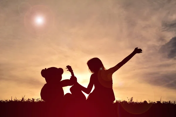 Silhouette fille jouer musical avec ours en peluche au coucher du soleil — Photo