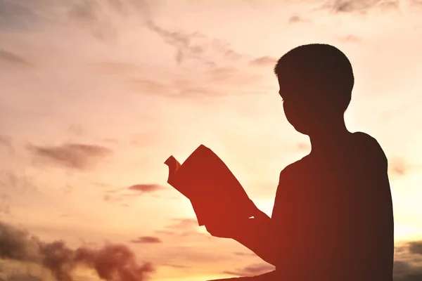 Silhouette a boy reading book on sunset