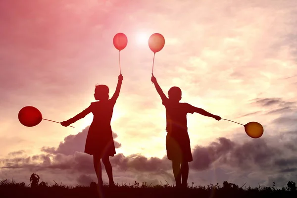 Crianças silhuetas com balão ao pôr do sol — Fotografia de Stock