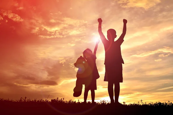 Silhouette enfants avec ours en peluche au coucher du soleil — Photo