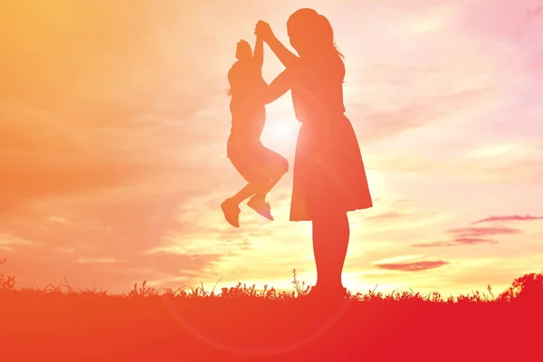 Silhuetter mor och lilla dotter spelar vid solnedgången — Stockfoto