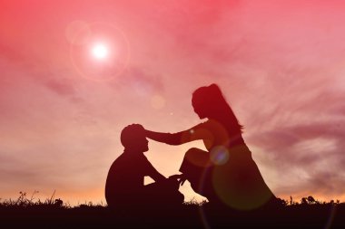 Bir çocuk ve annesi kalp şekli günbatımı üzerinde tutarak siluet
