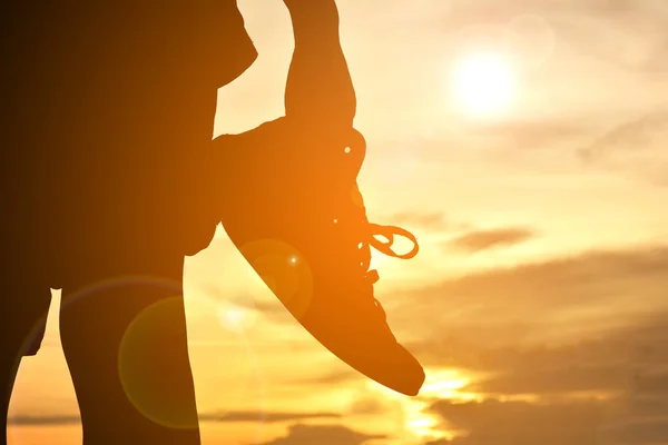 Silhouette garçon tenant des chaussures en toile sur le coucher du soleil — Photo