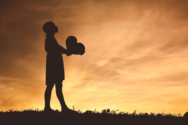 Silueta chica sosteniendo la forma del corazón al atardecer — Foto de Stock