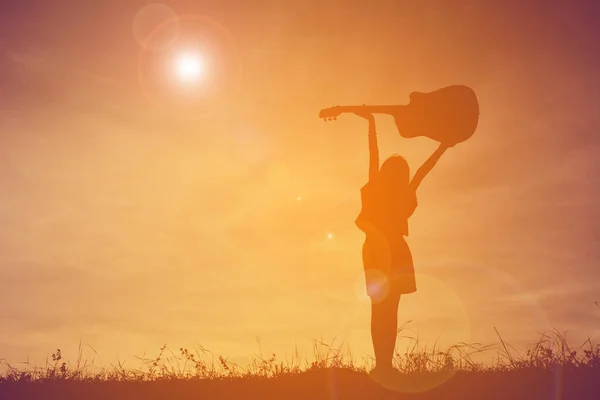 Silhouette fille heureuse jouant de la guitare au coucher du soleil ciel, temps heureux — Photo