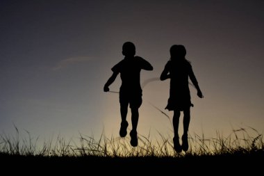 Siluet çocuklar ip atlama üzerinde gökyüzü günbatımı. 