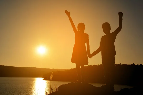 Silhouette of children open hand on the rock in river at the sky sunset — Stock Photo, Image