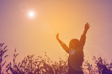 Mutlu kadın açık el gökyüzü günbatımı, çim alandaki silüeti