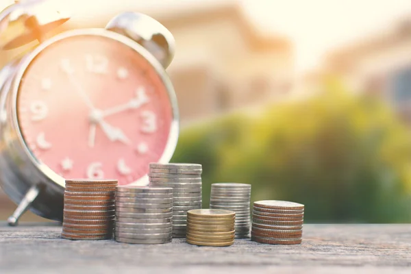 Moneda con reloj despertador en madera vieja y fondo de la casa grande, un color del concepto de tono vintage tiempo para ahorrar dinero — Foto de Stock