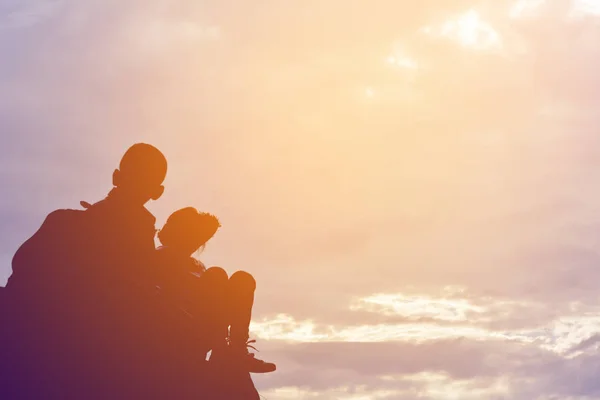 Silhouette of girl and boy on rock at the sky sunset — Stock Photo, Image