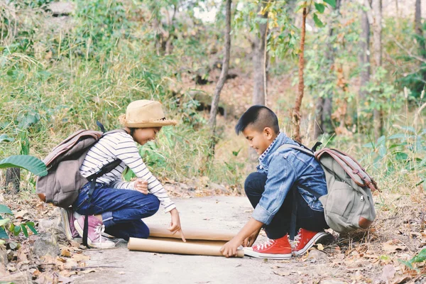 Gelukkige Aziatische kinderen op zoek een kaart, rugzak op natuur achtergrond — Stockfoto