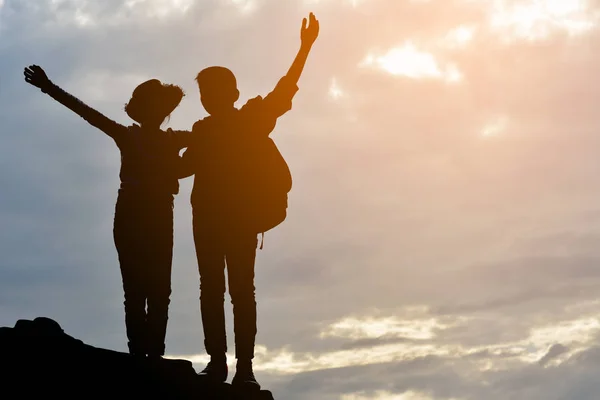 Silhueta de menina e menino na rocha no pôr do sol céu — Fotografia de Stock