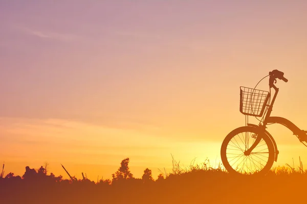 Σιλουέτα του ποδηλάτου στο χορτάρι με το ηλιοβασίλεμα του ουρανού — Φωτογραφία Αρχείου