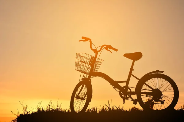 Σιλουέτα του ποδηλάτου στο χορτάρι με το ηλιοβασίλεμα του ουρανού — Φωτογραφία Αρχείου