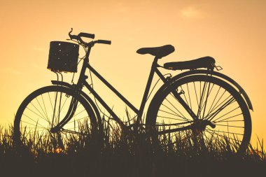 Eski gökyüzü günbatımı ile çimenlerin üzerinde bisiklet siluet