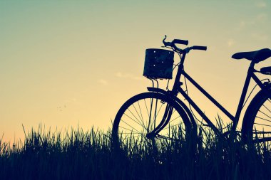 Eski gökyüzü günbatımı ile çimenlerin üzerinde bisiklet siluet