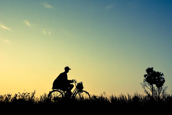 Silhouette dell'uomo e vecchia bicicletta sull'erba con il tramonto del cielo , — Foto Stock