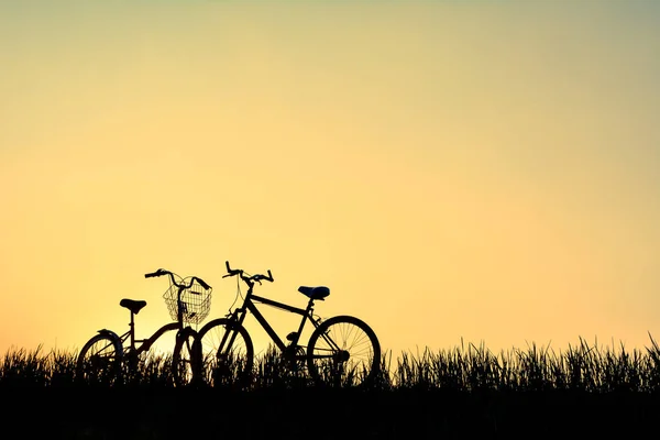 Silueta de bicicleta sobre hierba con la puesta de sol del cielo — Foto de Stock