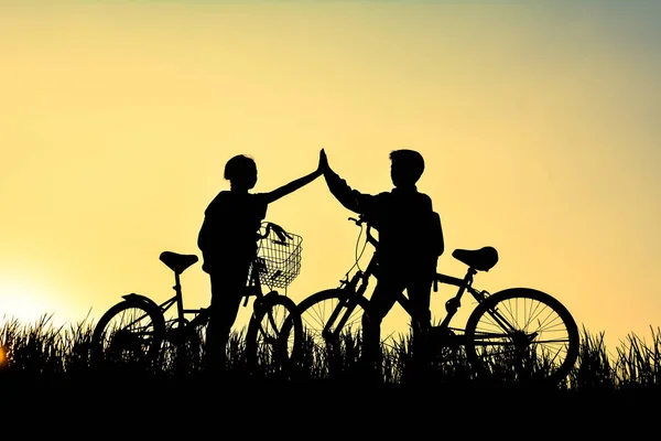 Silueta de niños con bicicleta en el campo de hierba — Foto de Stock