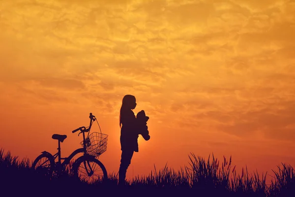 Silhouette of girl with bicycle on grass field at the sky sunset — Stock Photo, Image